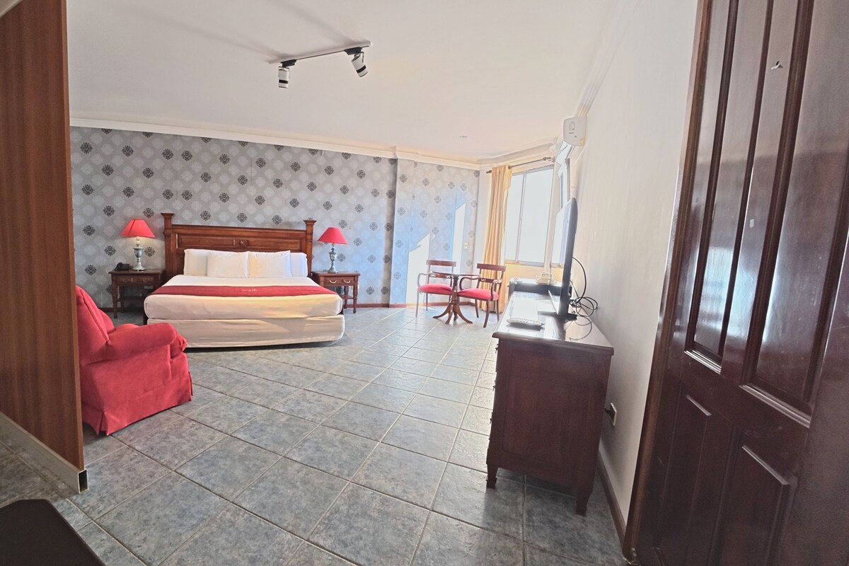 Una habitación de hotel con cama, escritorio, silla, lámpara y ventana.