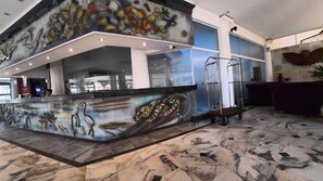 Rebedor amb sòl de marbre, taulell de recepció amb un mural i zona d'estar morada.