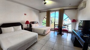 Habitación de hotel con dos camas, televisión, una mesita y balcón con vistas.
