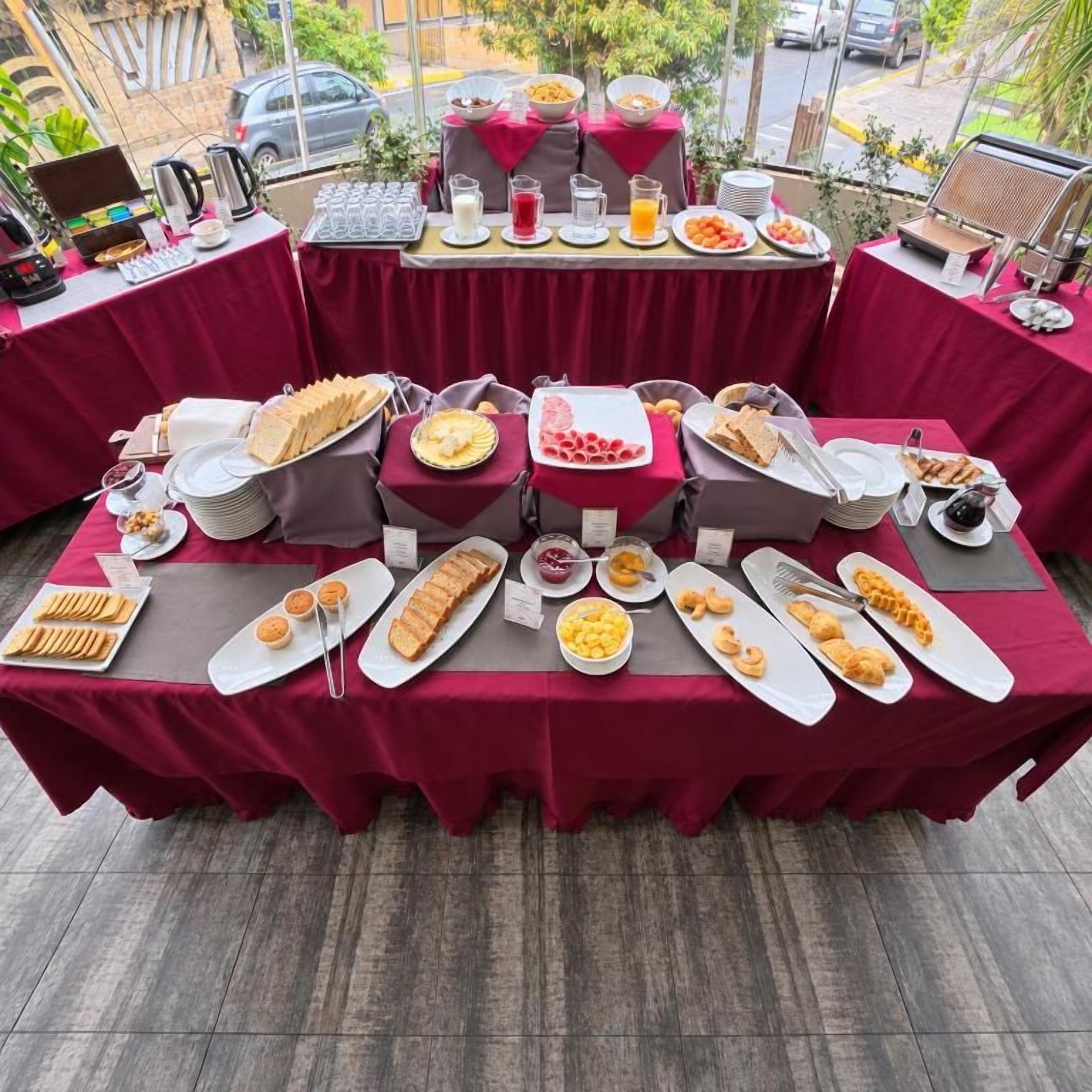 Una mesa de buffet con diversos alimentos y bebidas, ubicada al aire libre con vista a la calle.
