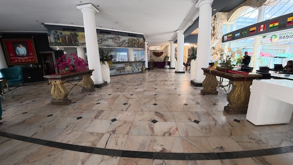 Un vestíbulo con suelo de mármol, columnas blancas y una recepción.
