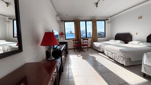 Una habitación de hotel con dos camas, un escritorio con lámpara, una silla y un ventanal con cortinas.