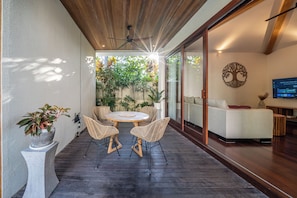 A modern patio with a round table and wicker chairs, a white sofa, and a TV mounted on the wall.