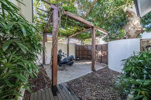 A covered outdoor area with a wooden pergola, a scooter, and a white wall.