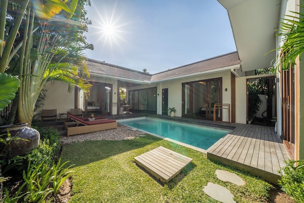 A modern house with a swimming pool, outdoor seating, and lush greenery.