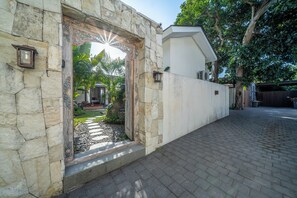 A stone entrance with a decorative archway, a paved pathway, and a white wall with a security camera.