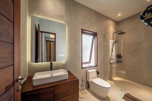 Een moderne badkamer met een houten wastafelmeubel, een grote spiegel, een toilet en een douche met glazen wanden.