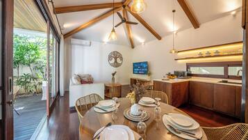 A modern kitchen with wooden beams, a dining table set for four, and a television mounted on the wall.
