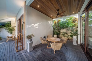 Un patio exterior con terraza de madera, mobiliario de mimbre y plantas en macetas.