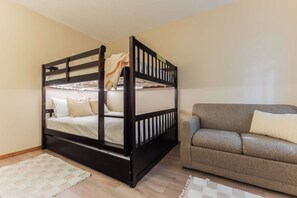 A bunk bed with a headboard, a grey sofa, and a patterned rug in a room with wooden flooring.