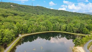 Um lago rodeado por floresta densa, com uma trilha para caminhada e um pequeno coreto.