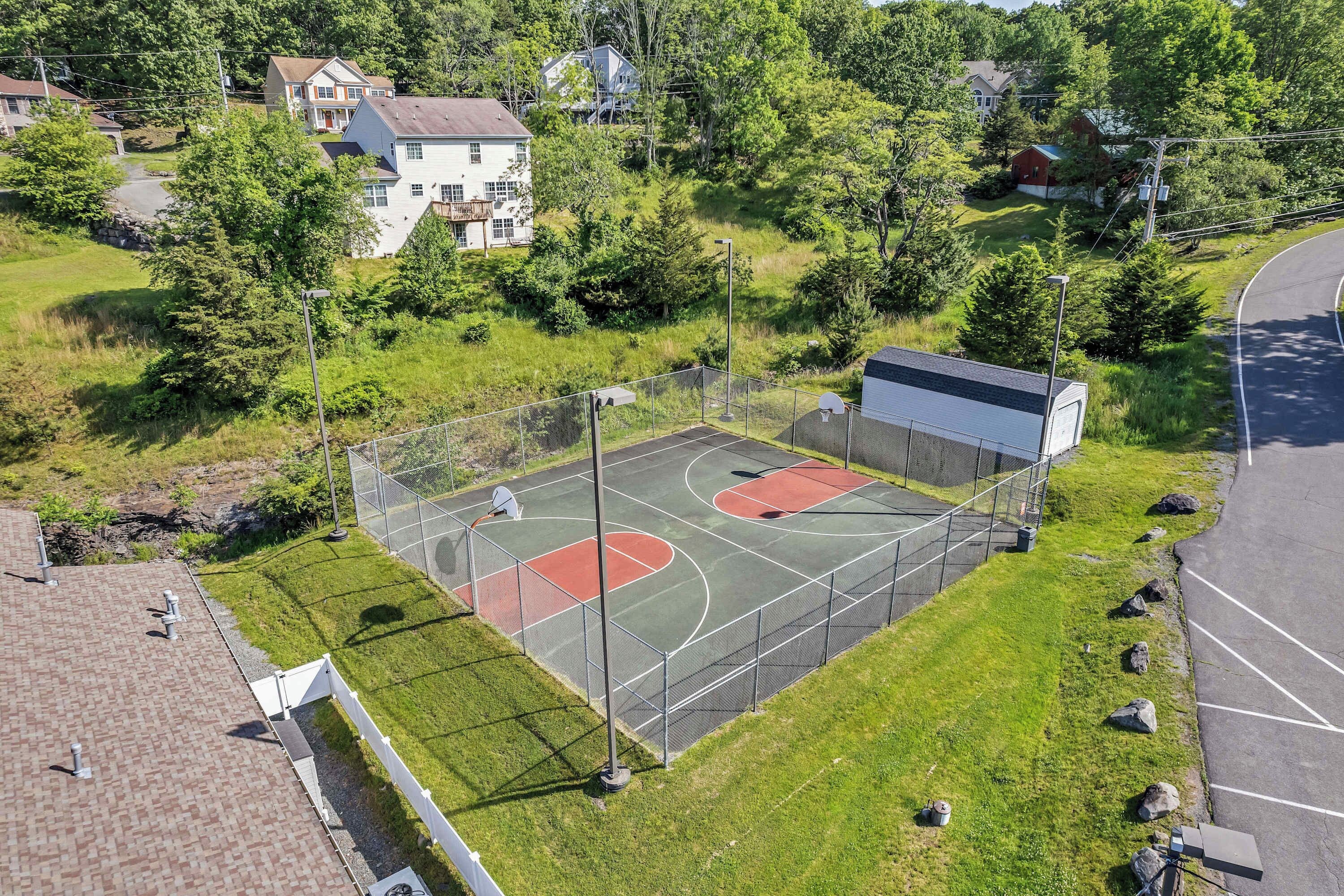Una cancha de baloncesto exterior con valla, rodeada de césped y árboles.