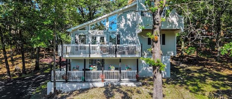 A two-story house with a balcony, surrounded by trees.