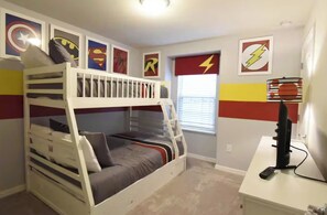 A bunk bed room with superhero-themed wall art, a desk with a computer, and a window with blinds.