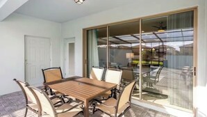 Ein Essbereich mit Holztisch und -stühlen, einer Schiebetür aus Glas, die auf eine Terrasse im Freien führt, und einem Deckenventilator.