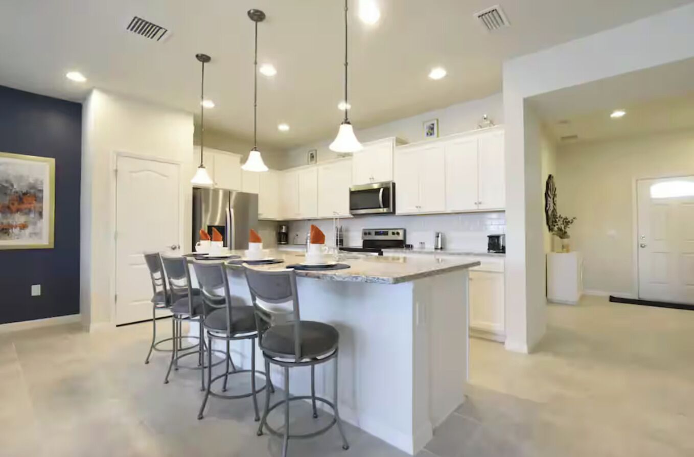 A modern kitchen with white cabinets, a central island with bar stools, pendant lighting, and a microwave.