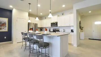 A modern kitchen with white cabinets, a central island with bar stools, pendant lighting, and a microwave.
