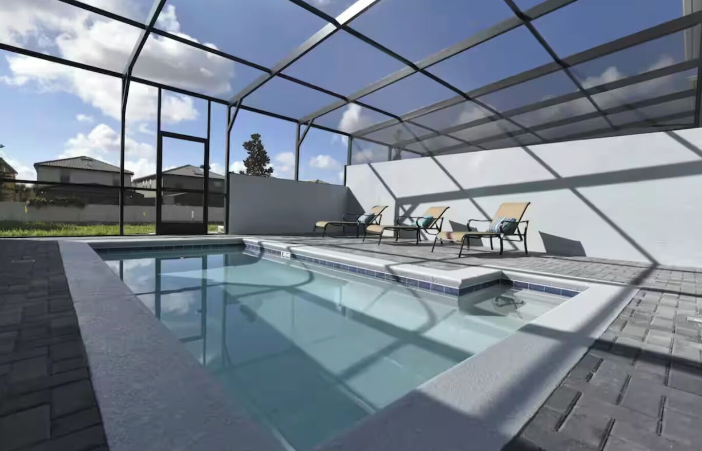 A modern outdoor swimming pool with a glass enclosure, lounge chairs, and a clear view of the surrounding area.