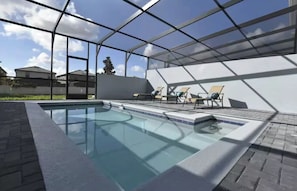 A modern outdoor swimming pool with a glass enclosure, lounge chairs, and a clear view of the surrounding area.