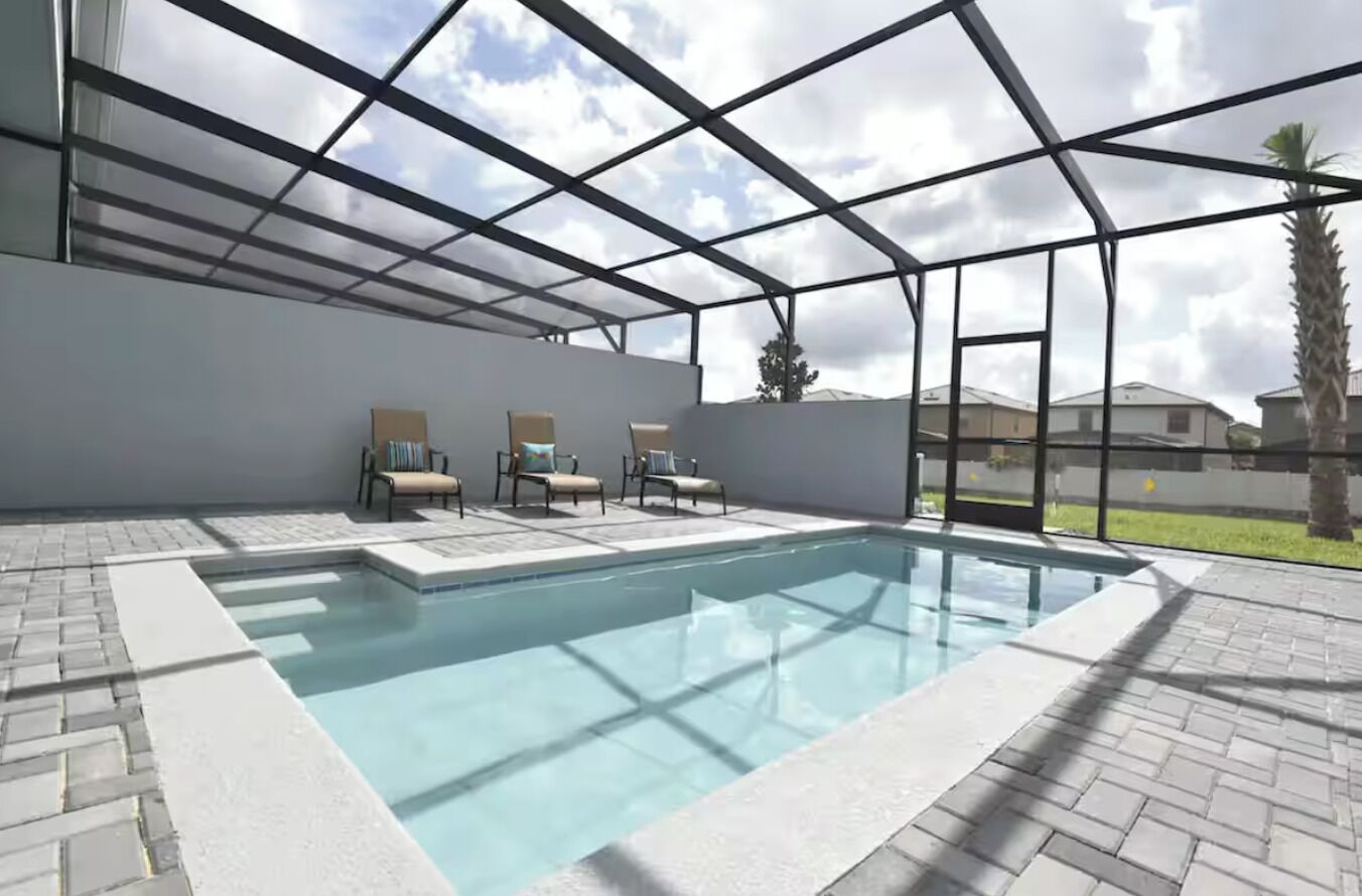 A swimming pool with a glass enclosure, surrounded by lounge chairs and a paved deck.