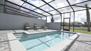 A swimming pool with a glass enclosure, surrounded by lounge chairs and a paved deck.