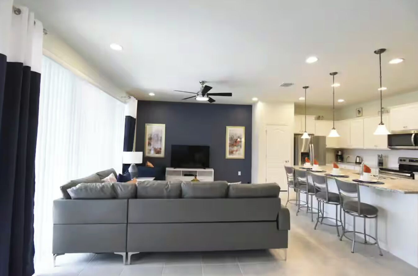 A modern living room with a grey sofa, a flat-screen TV, and a ceiling fan.