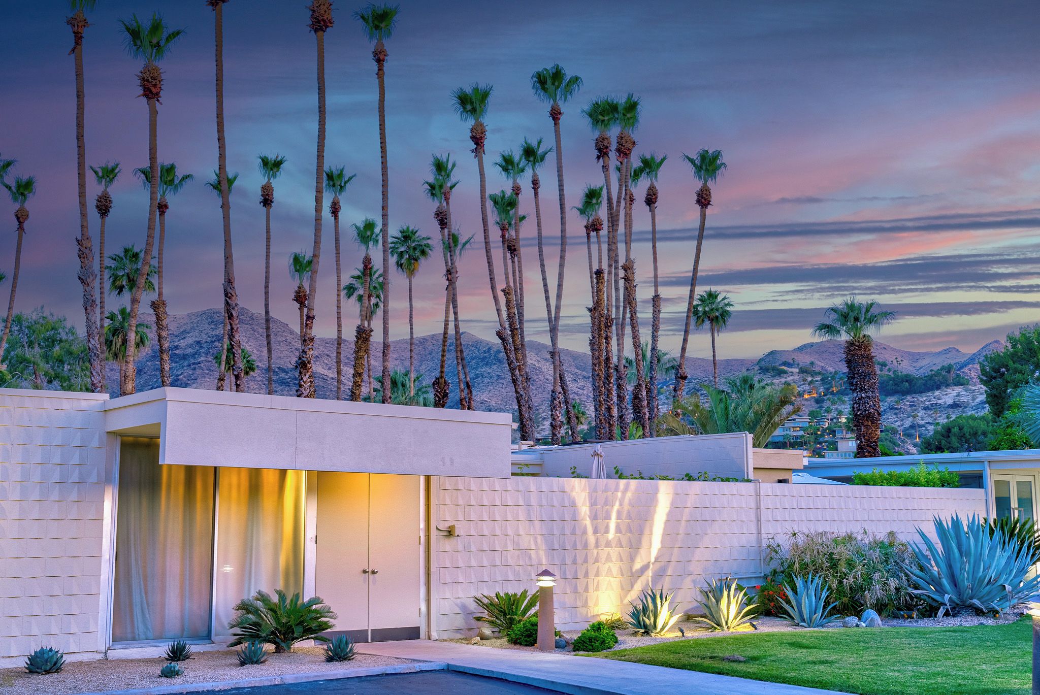 A modern house with a pool, surrounded by palm trees and a mountainous backdrop.