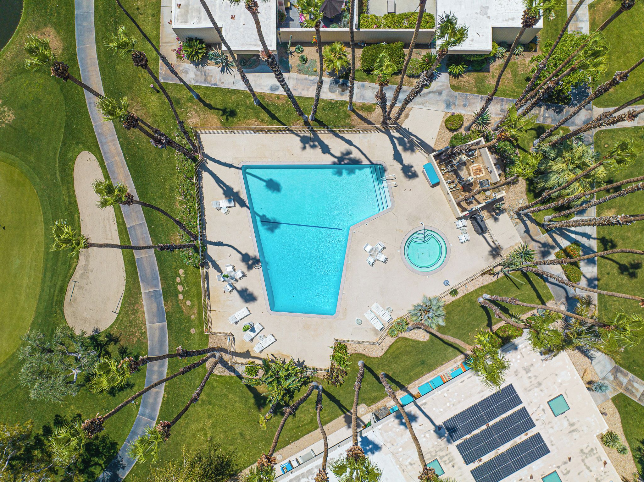 An aerial view of a resort with a large swimming pool, sun loungers, and palm trees.