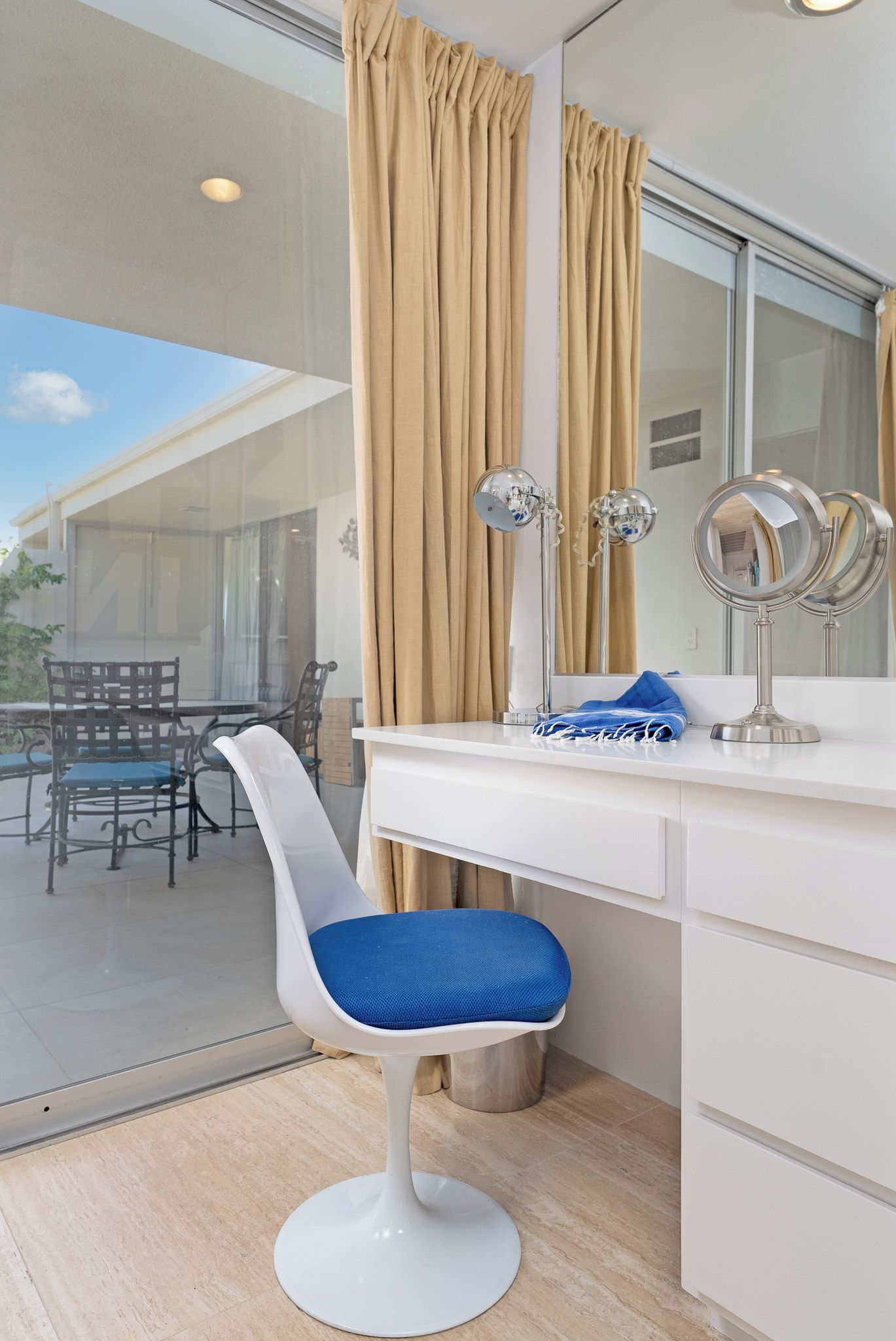 Een badkamer met een wit wastafelmeubel, een blauwe stoel en een grote spiegel.