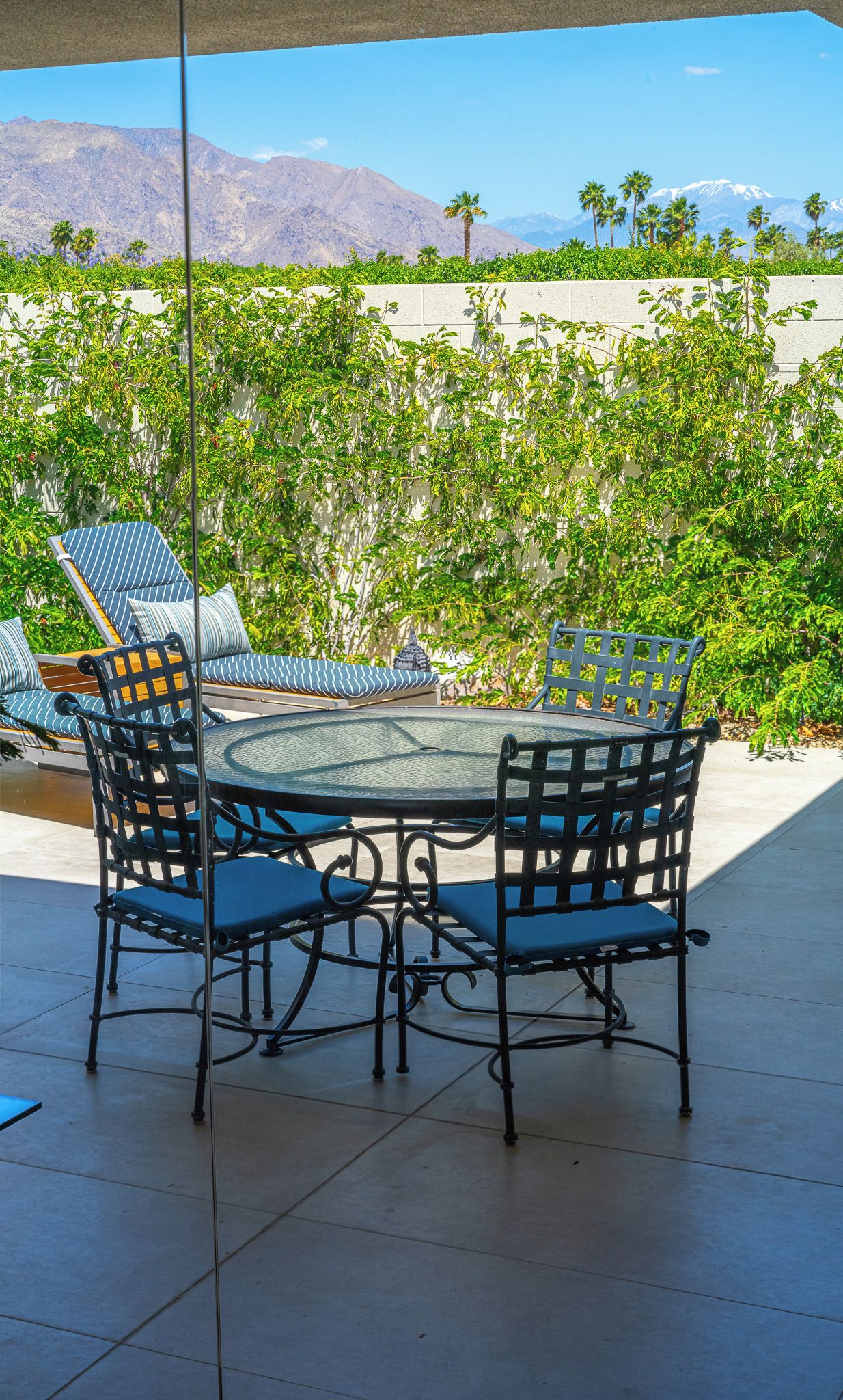 Une terrasse avec une table ronde et quatre chaises, entourée d’un mur blanc et d’une végétation luxuriante.