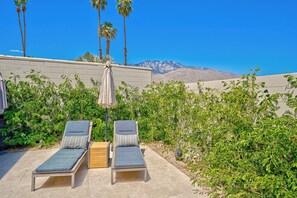Une terrasse avec deux chaises longues et une table, entourée de verdure et offrant une vue sur la montagne.