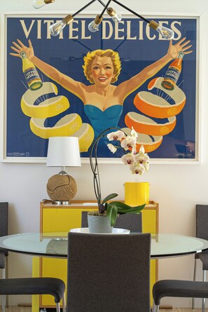 Quarto com pôster de uma mulher segurando garrafas, uma luminária e uma planta em um armário amarelo.