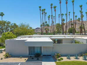 A modern building with a flat roof, surrounded by palm trees and a mountainous backdrop. - Seven Lakes Golf and Country Club 2 bedroom plus Den bungalow (Palm Springs)