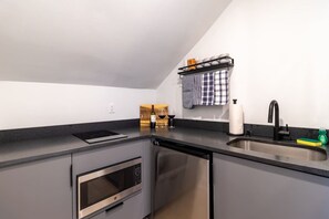 Uma cozinha moderna com forno embutido, máquina de lavar louça, pia com torneira preta e uma garrafa de vinho sobre o balcão.