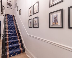 Uma escadaria com carpete azul e detalhes dourados, que leva a um patamar com quadros nas paredes.