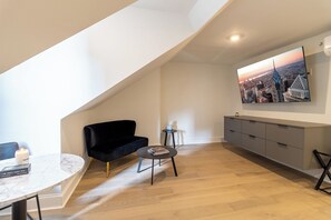 A modern living space with a black sofa, a round table, and a cityscape painting on the wall. - Thena Hotel - Spacious Studio (Philadelphia)