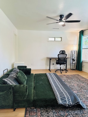 A room with a green sofa, a desk, a chair, a ceiling fan, and a patterned rug. - 5-bedroom 4 bath Pool  house near AT&T Stadium Arlington (Arlington)