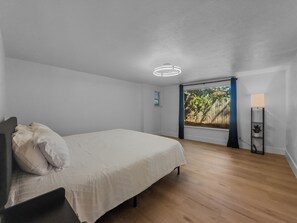 Ein Schlafzimmer mit einem Bett, einem Fenster mit Blick auf einen Holzzaun und einer Stehlampe.