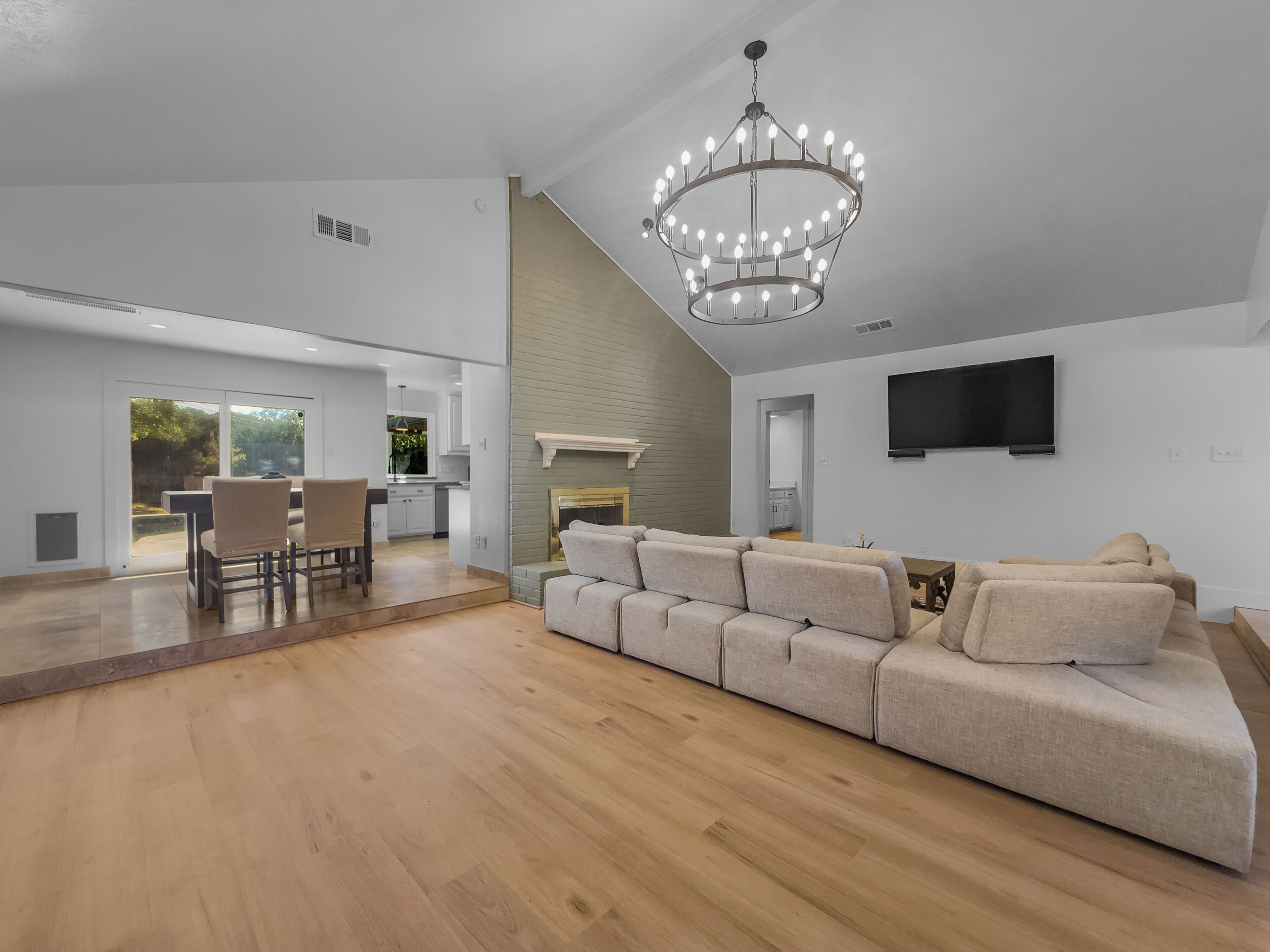 A spacious living area with a large sectional sofa, a dining table with chairs, a fireplace, and a modern chandelier.