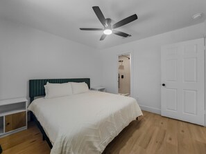 Une chambre à coucher comprenant un lit, une table de chevet, un ventilateur de plafond, une porte et un espace douche.