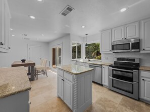 Une cuisine moderne avec des meubles blancs, des plans de travail en granit, un four encastré et une grande fenêtre donnant sur un paysage verdoyant.
