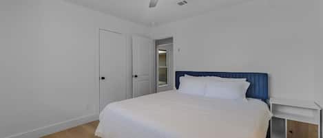 A bedroom with a bed, a nightstand, a ceiling fan, and a door.