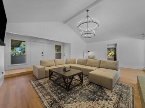 Un salon spacieux avec un grand canapé d’angle, une table basse et un lustre.