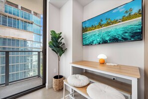 Ein modernes Wohnzimmer mit großem Fenster, Flachbildfernseher, Topfpflanze, Lampe und einem weißen Sofa.