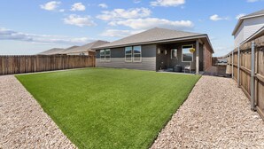 A residential property with a well-maintained lawn, a wooden fence, and a house with a grey exterior. - Premium  4BR Home Near Midland airport (Odessa)