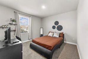 Un dormitorio con cama, escritorio, silla, televisor, ventana con cortinas y decoración en la pared.