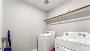 A laundry room with a washing machine, dryer, and a vacuum cleaner. - Premium  4BR Home Near Midland airport (Odessa)