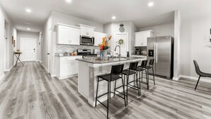 A modern kitchen with white cabinetry, a stainless steel refrigerator, and a central island with bar stools. - Premium  4BR Home Near Midland airport (Odessa)