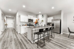 Una cocina moderna con armarios blancos, un refrigerador de acero inoxidable y una isla central con taburetes de bar.
