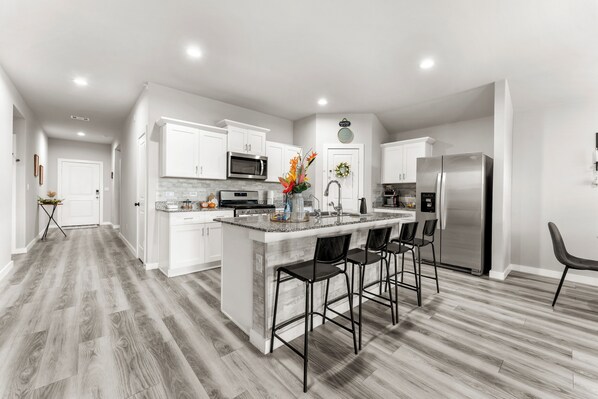 A modern kitchen with white cabinetry, a stainless steel refrigerator, and a central island with bar stools.
